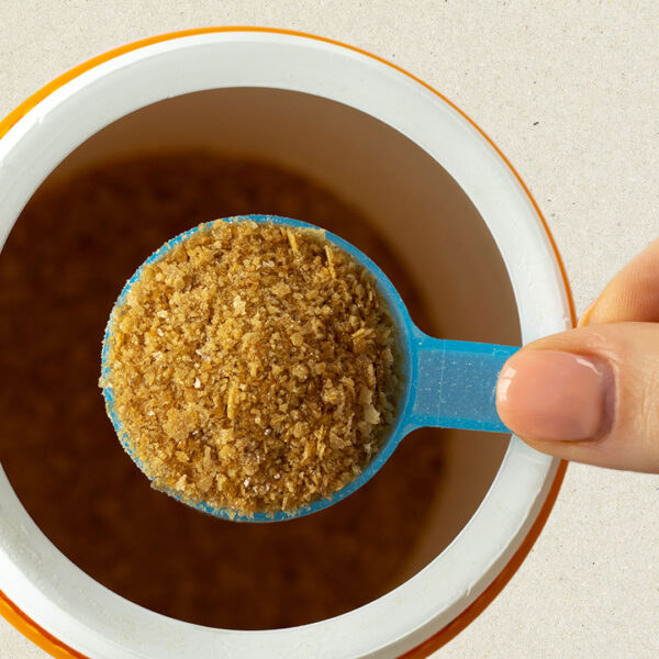 Hand holding a spoonful of bone broth poweder over a cup